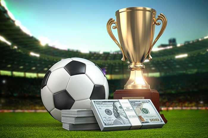 Trophy, a stack of money, and a soccer ball graphics at the front of a blurred stadium.