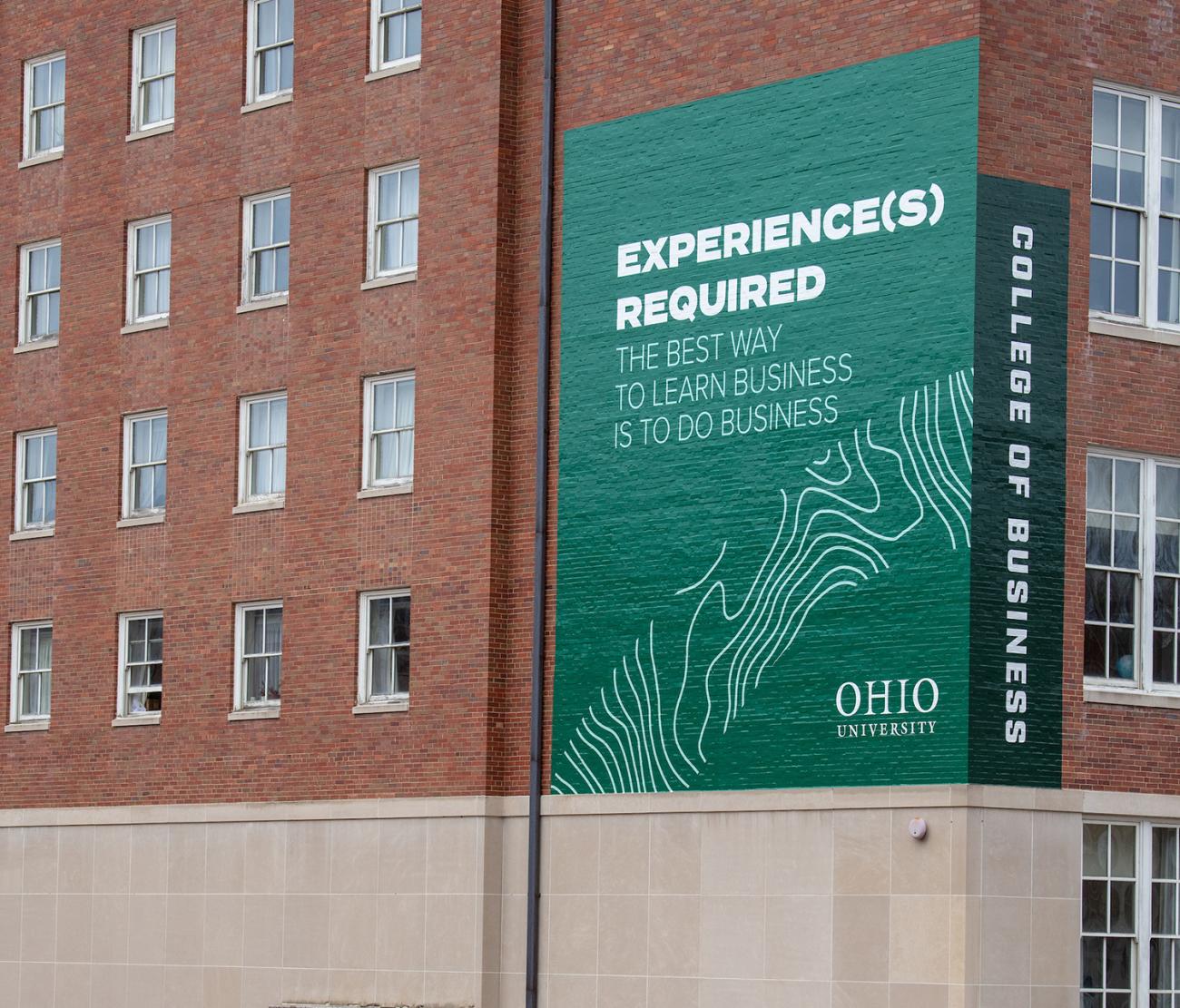 Side of Copeland Hall in Athens, Ohio. Banner reads "Experience(s) Required: The best way to learn business is to do business" 