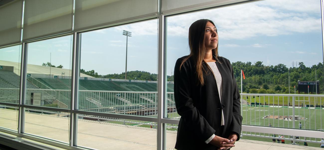 Sports Administration student stands in the Ohio University football stadium wearing a suit