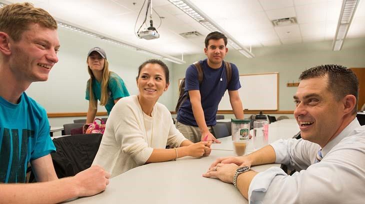 Students talk with a professor in a classroom