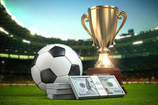 Trophy, a stack of money, and a soccer ball graphics at the front of a blurred stadium.