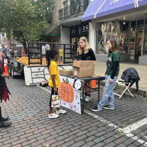 2 students handing out candy to a child at Community Halloween Block Party