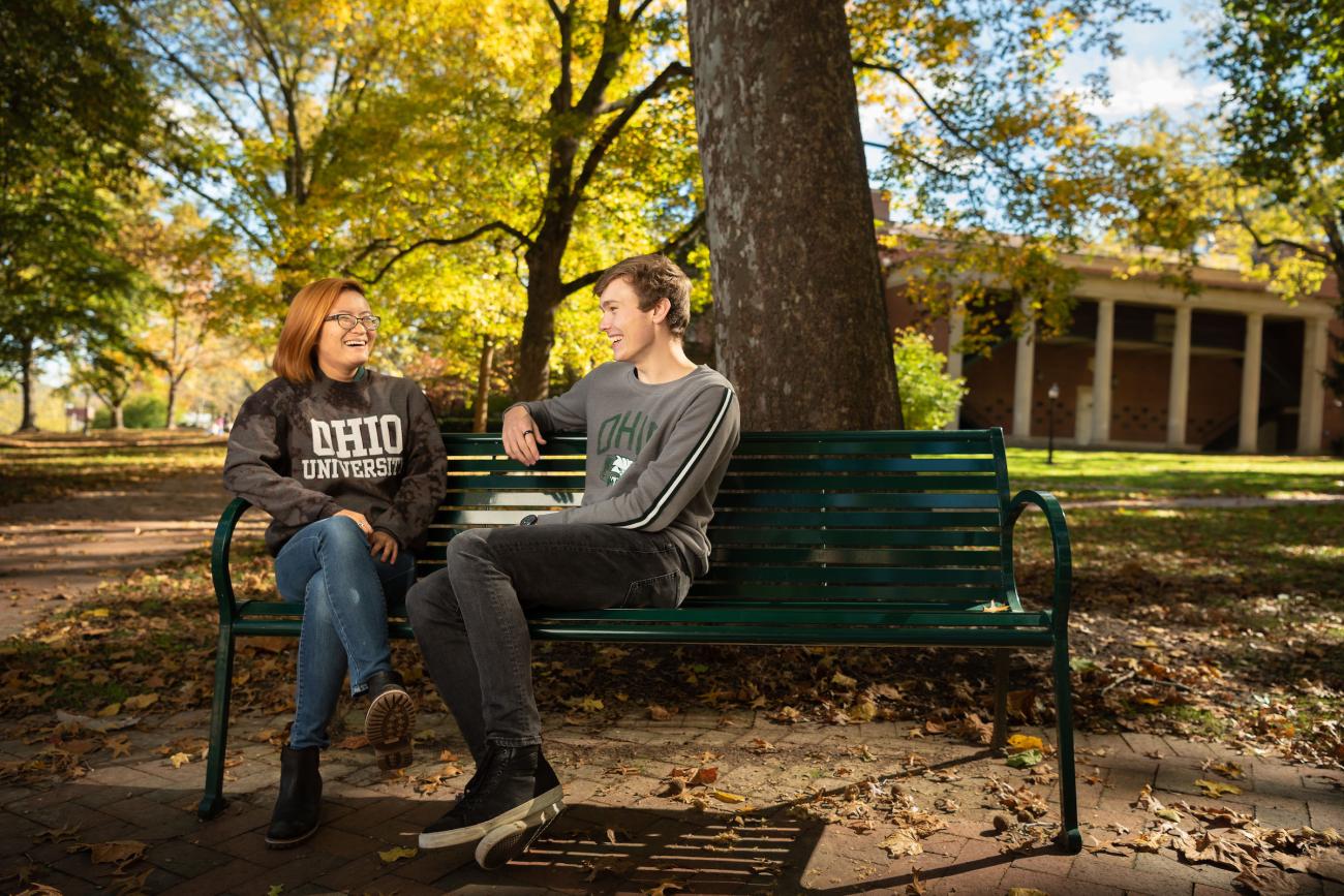 Two students conversing on a bench on College Green.