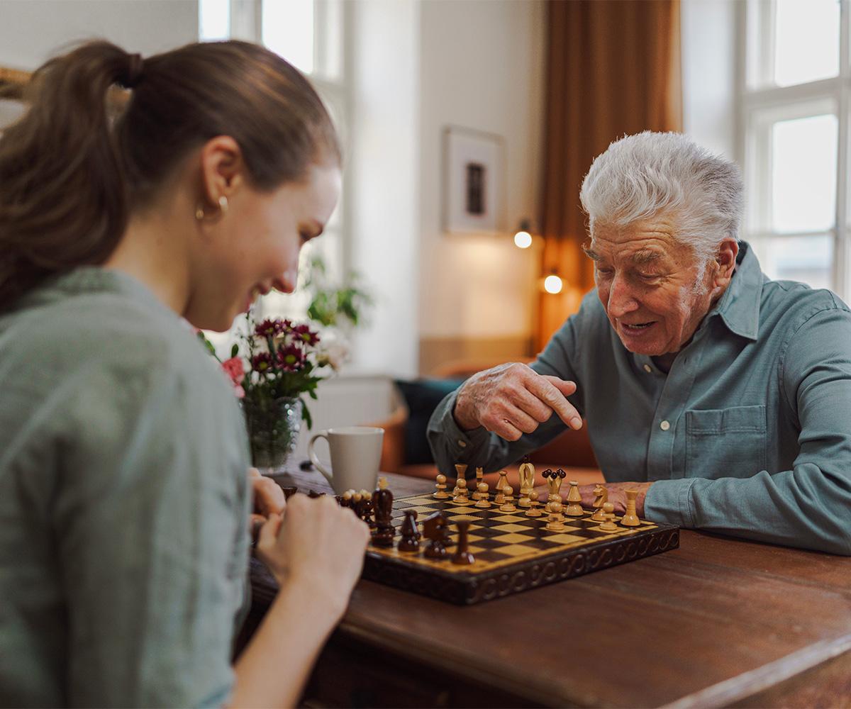 A stock image of a young adult playing chess with an elderly person.