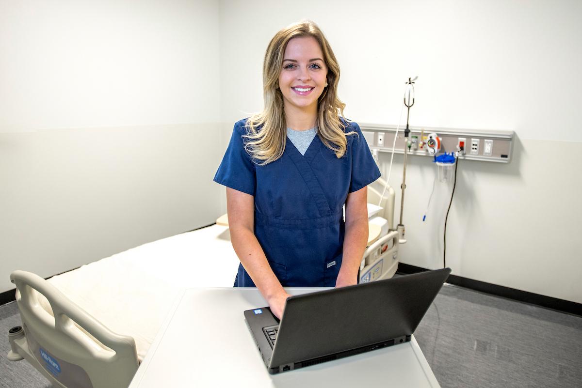 Integrated Healthcare Studies student works on a laptop in a hospital exam room