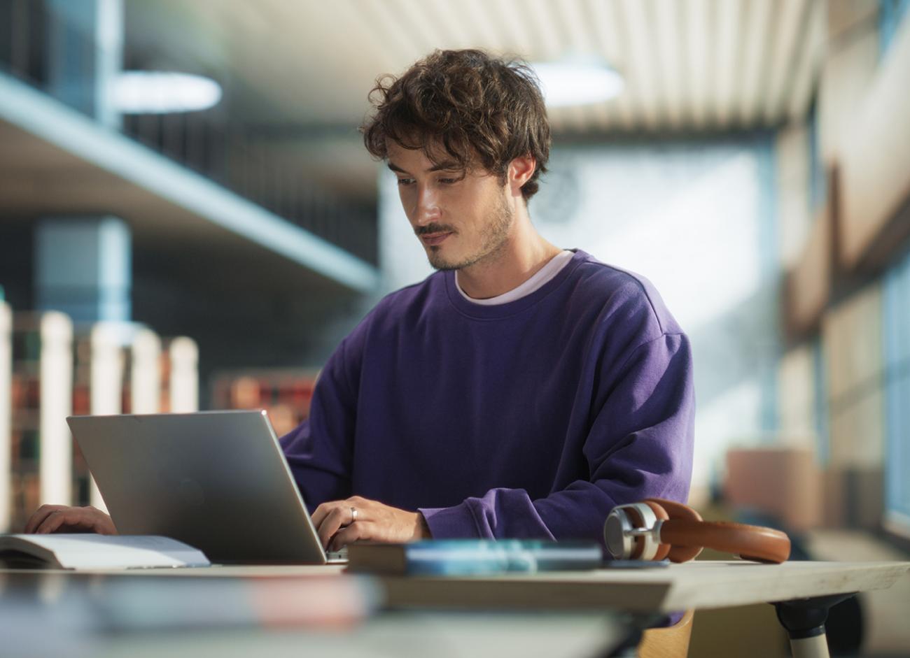 A man sitting at a desk with a laptop and notebook next to him.