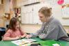 Teacher listening to young female student reading.