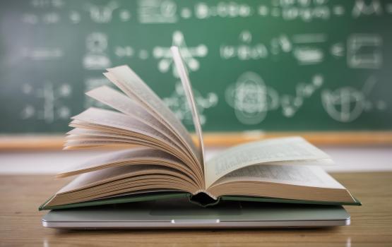 Open book sitting on a laptop in front of a chalkboard.
