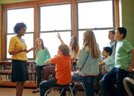 Teacher talking with middle school students in a classroom.