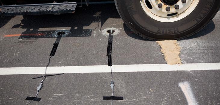Cables taped to a road surface extending into small circular holes in the road