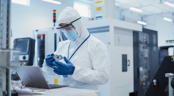 Engineer in protective gear standing at workstation inspecting micro nano device