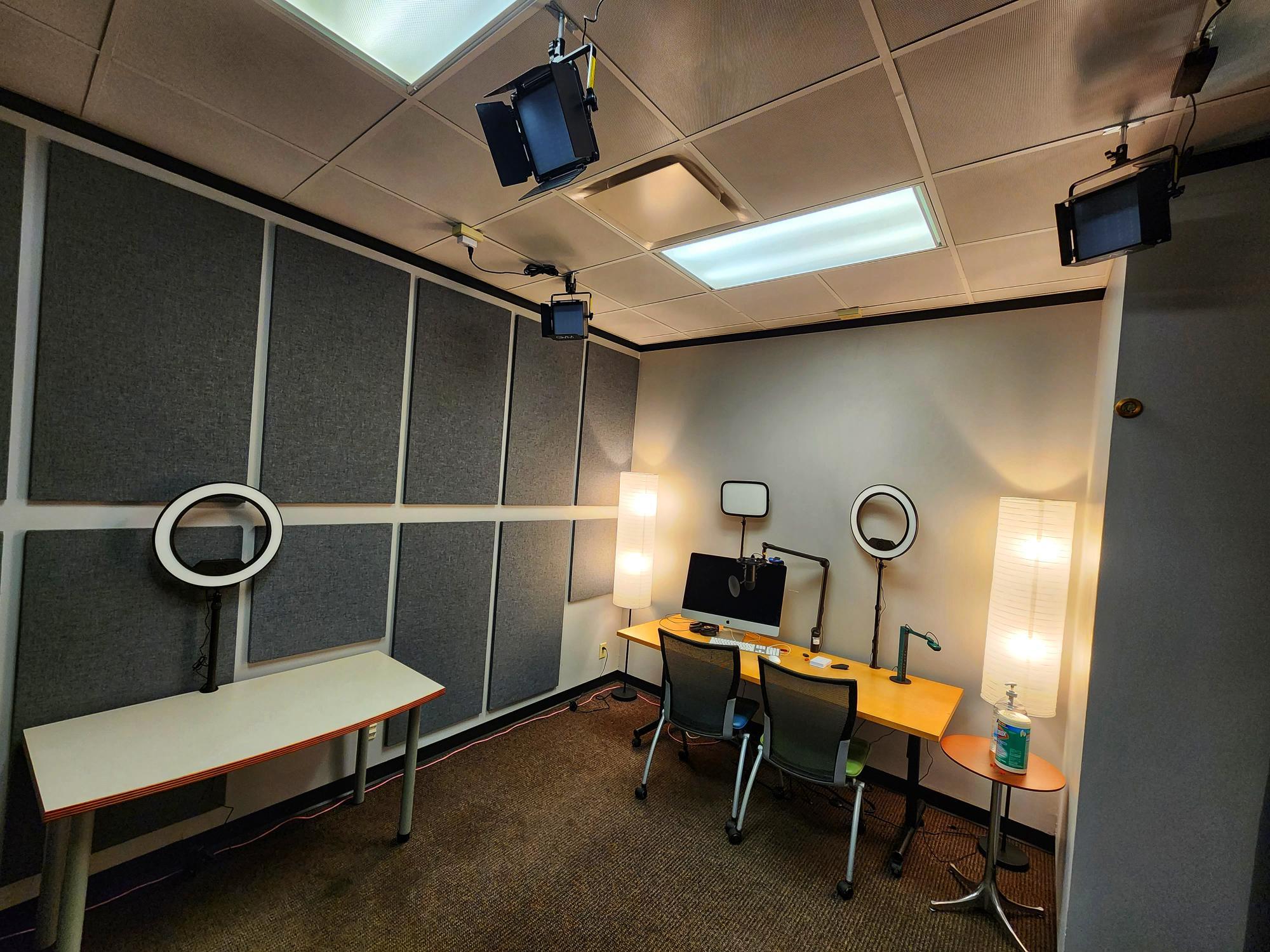 A room with a iMac computer, video lights, desk, sound boards on the walls.