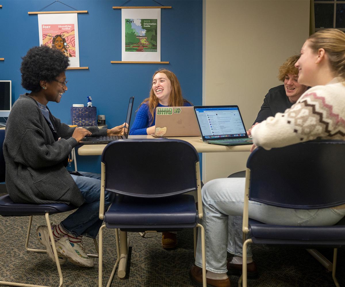 Students talk together while working at laptops
