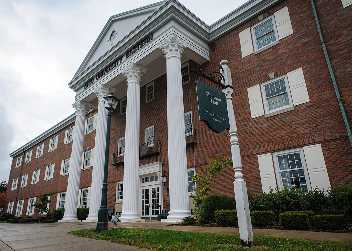 A three-story brick building with a white column entrance the windows have white shutters.