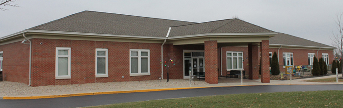 A brick building with brick columns at the entrance and tall windows and a grey roof.