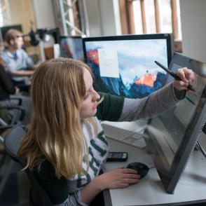 girl writing on digital display aside a computer screen