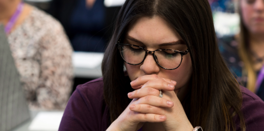 Person with eyes closed and hands clasped near mouth.