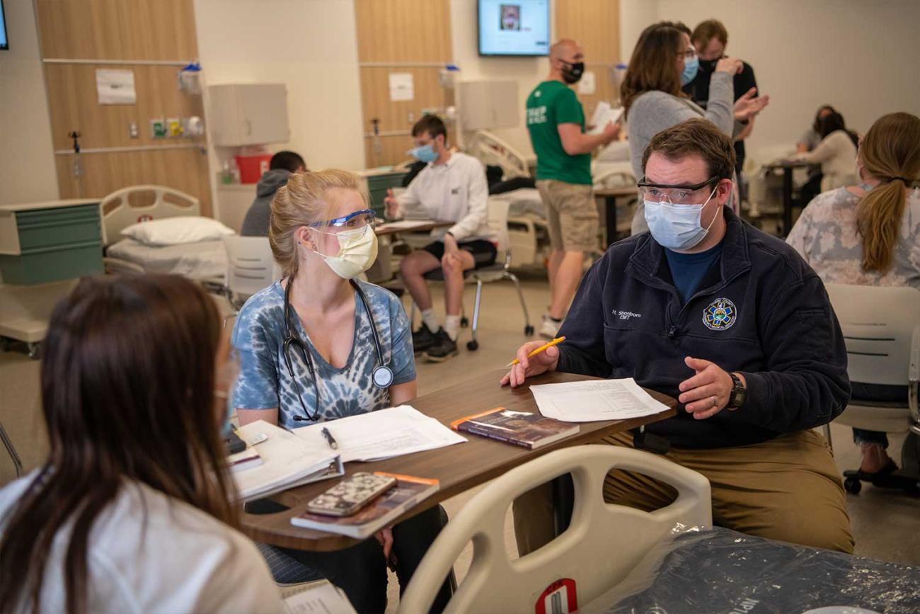 Focusing on two nursing students and a teacher in an exam room sitting at a table with papers