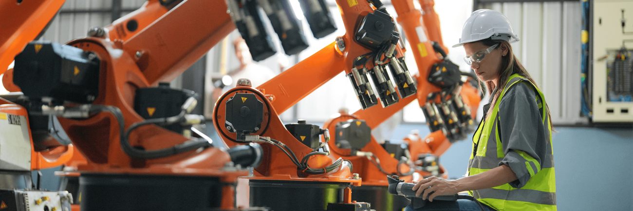 person in yellow vest stands in front of large orange machinery