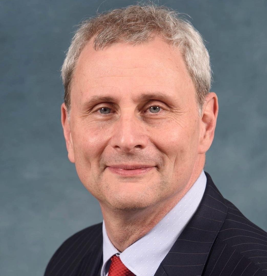 Don Leo shown from head to shoulders wearing a dark suit and red tie