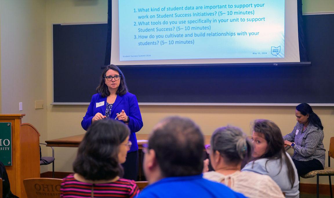 A woman stands in the front of a small auditorium to facilitate small group discussions