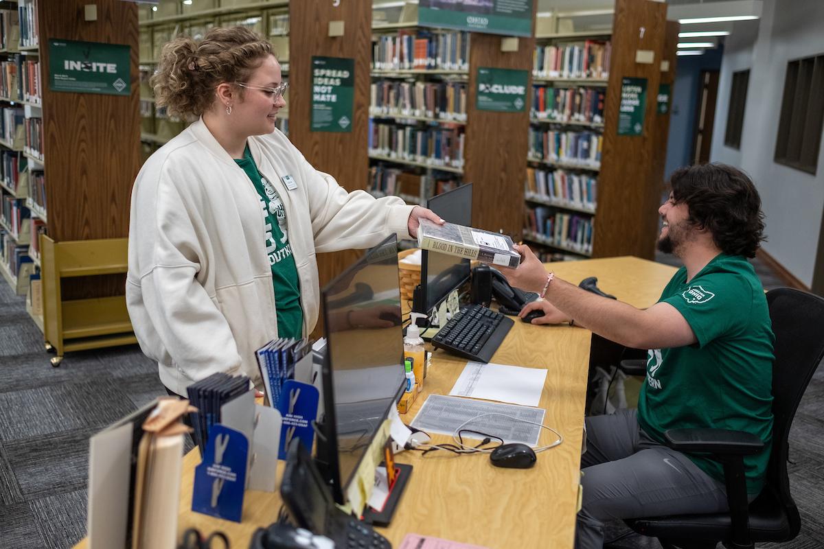student being handed a book from the library desk