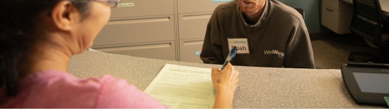 Close up of a new member signing paperwork with a WellWorks staff member behind the desk.