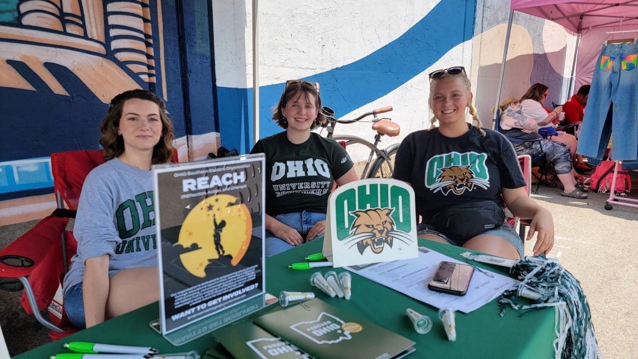 Three students in Ohio University shirts sitting at table outdoors