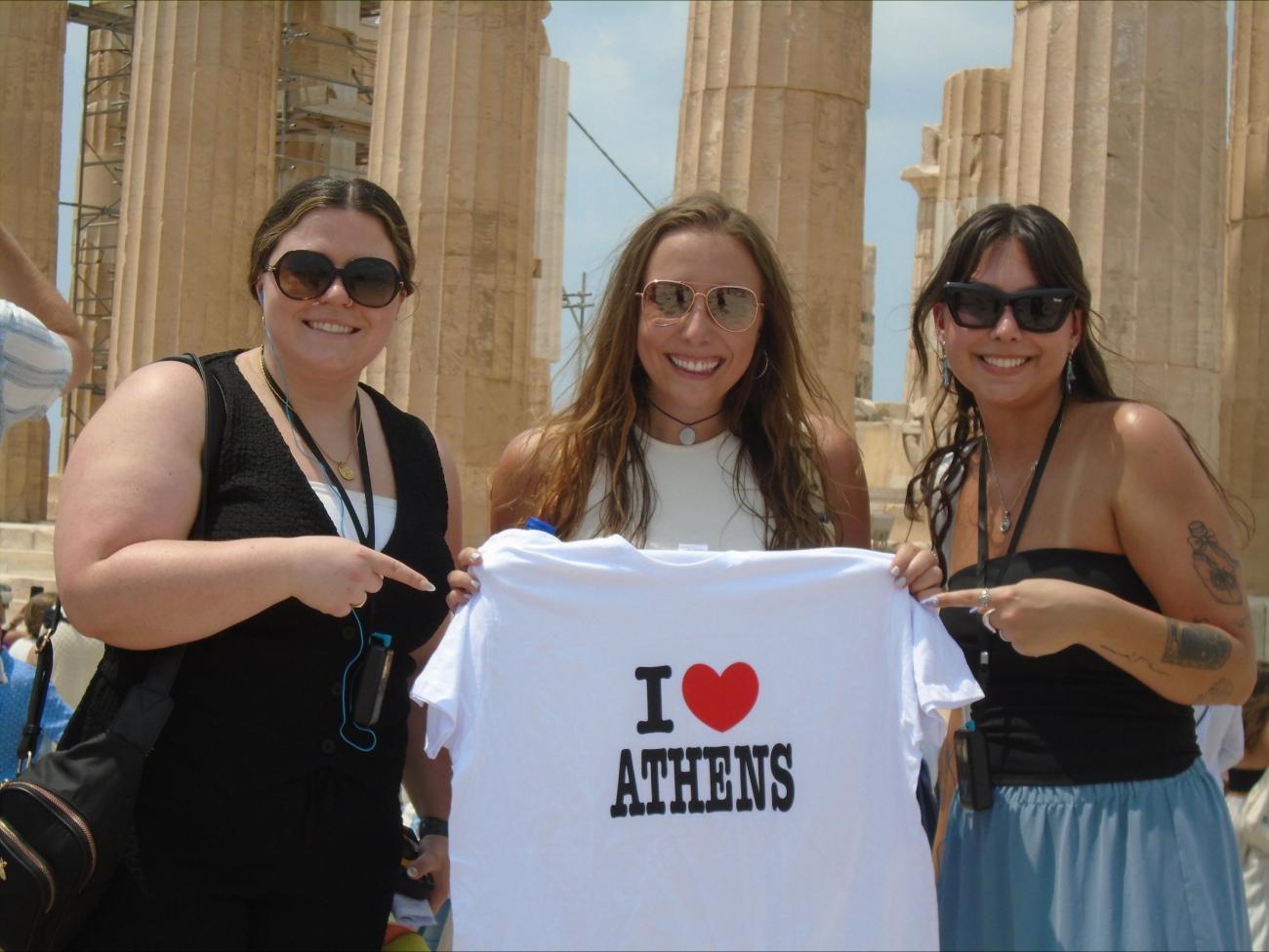 Three girls holding white t-shirt that says I "heart" Athens.