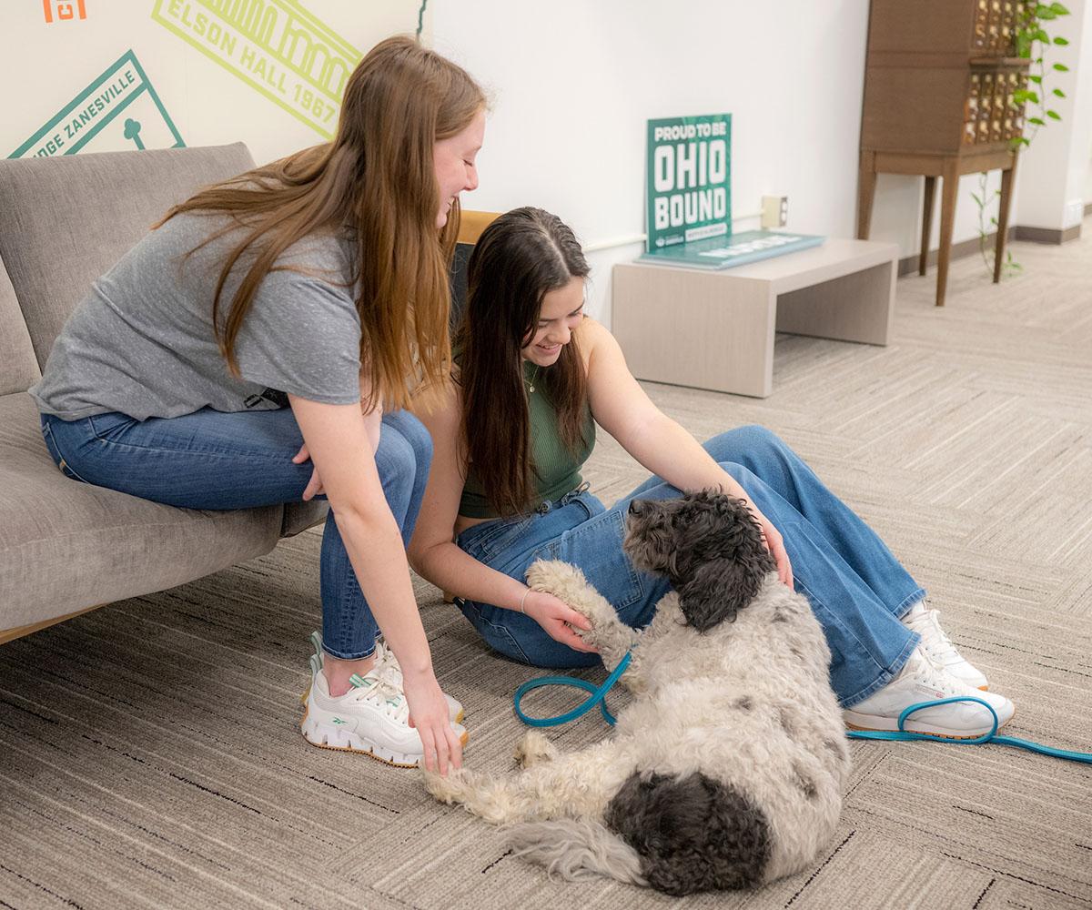 Two students play with a dog during a mental health event.