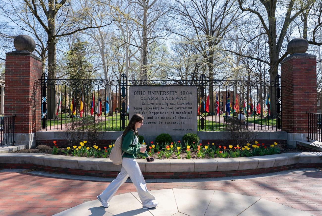 woman walks in front of the college gateway on Ohio University's main campus