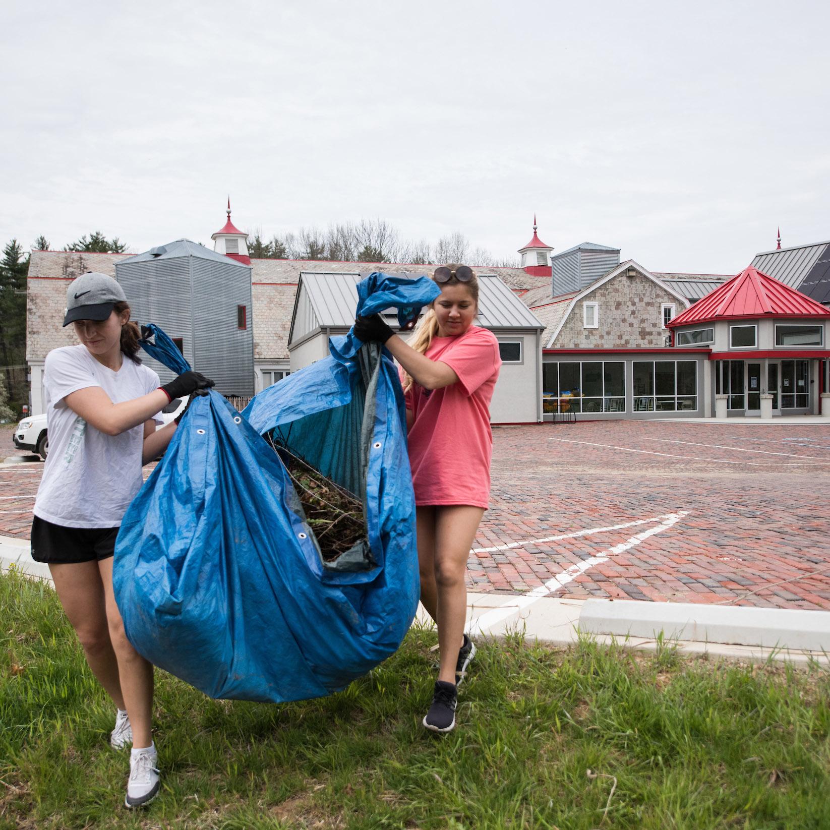Two students carrying sticks and other debris on a tarp