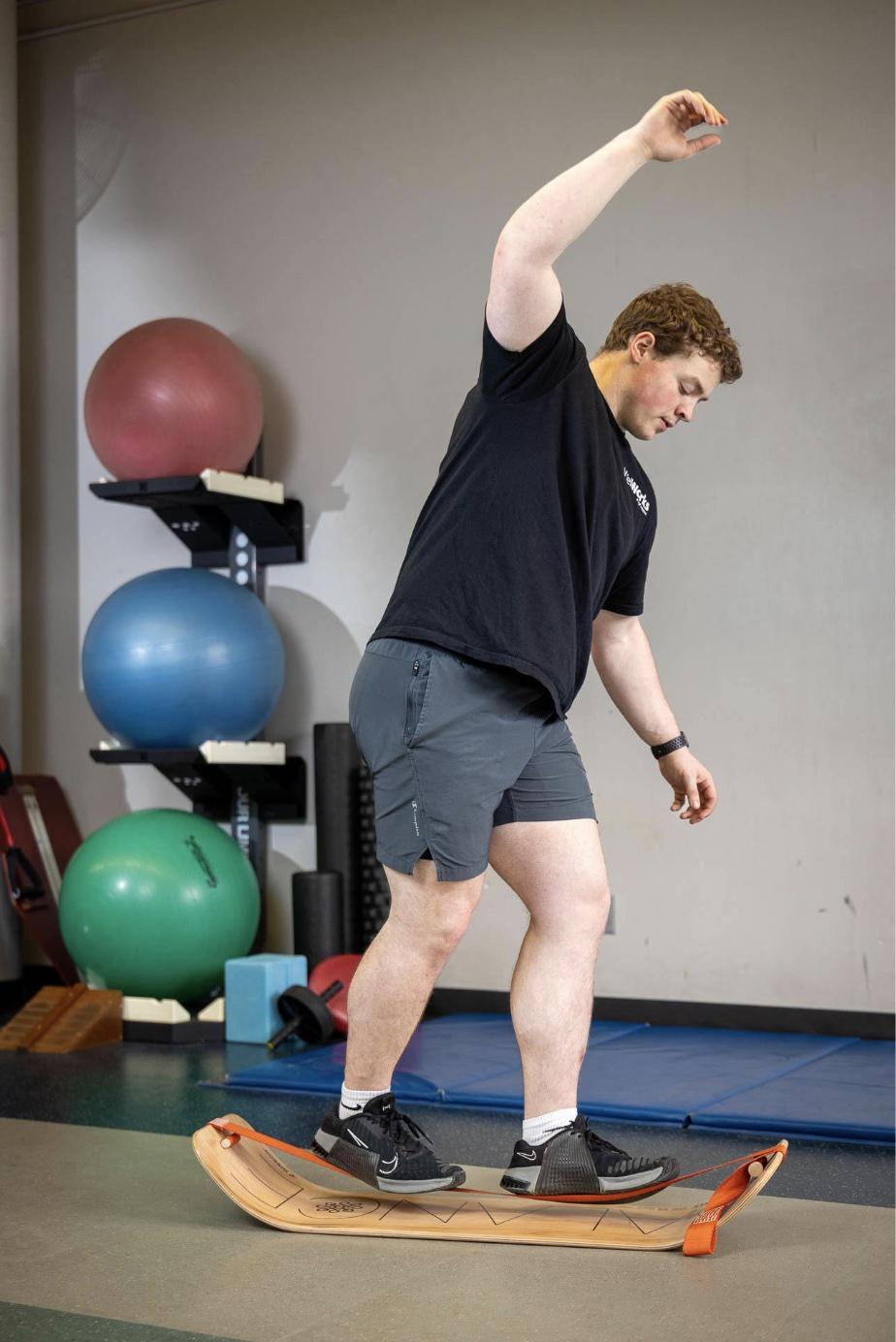 WellWorks member standing on a balance board with yoga balls in the background