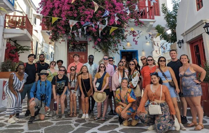 Group photo in front of beautiful Greek building covered in flowers.
