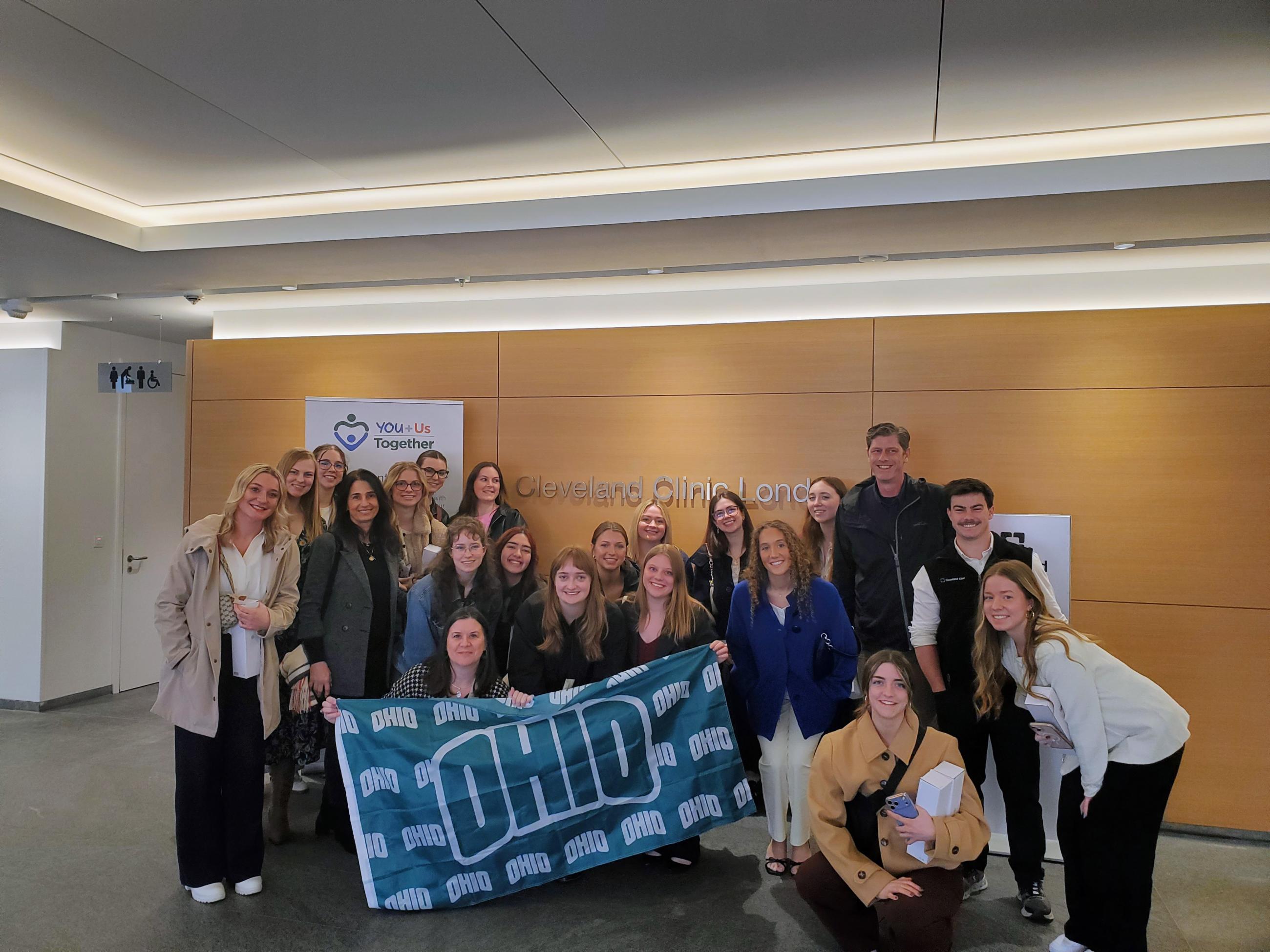 A group of Ohio University students and faculty pose with an OHIO flag at the Cleveland Clinic in London