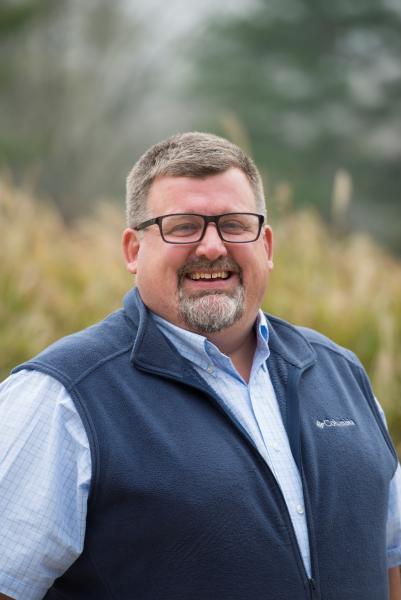 Photo of Joe Wakeley looking straight at the camera. Joe is standing in front of a field.