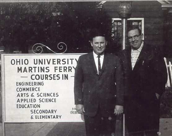 Two men in suits standing next to a sign in the 1960'2