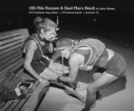 A runner bending over looking at leg of other runner sitting on bench.